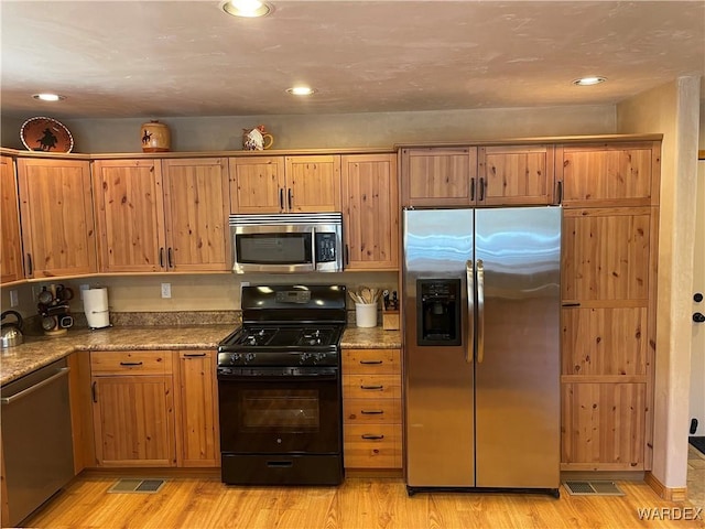 kitchen featuring light stone countertops, appliances with stainless steel finishes, brown cabinetry, and light wood-style floors