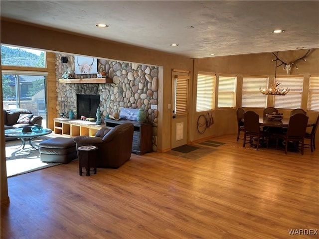 living area featuring a stone fireplace, recessed lighting, wood finished floors, and a notable chandelier