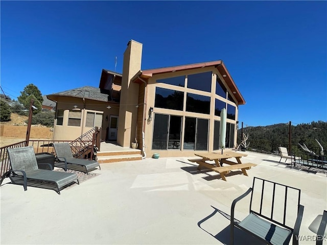 back of house featuring a chimney, a patio area, and stucco siding