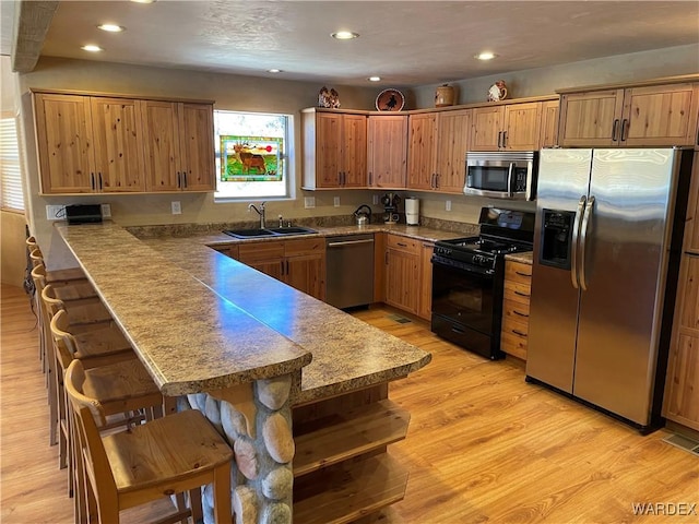 kitchen with a breakfast bar area, stainless steel appliances, a peninsula, a sink, and brown cabinets