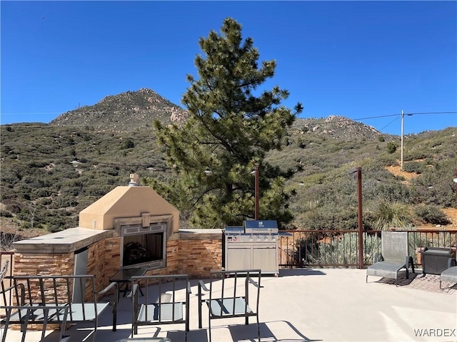 view of patio with exterior kitchen, a fireplace, fence, and a mountain view