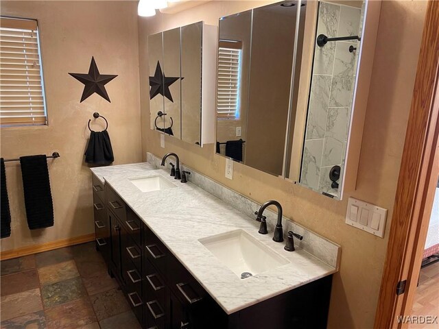 full bath with double vanity, stone tile floors, a sink, and baseboards