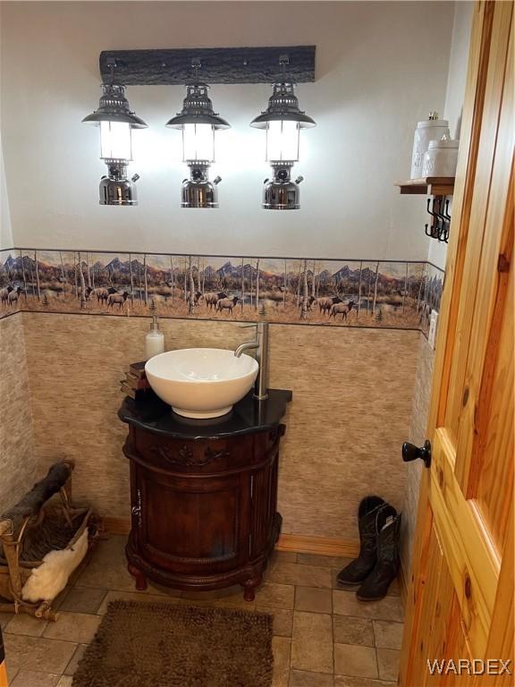 bathroom featuring a wainscoted wall, tile walls, stone tile flooring, and vanity