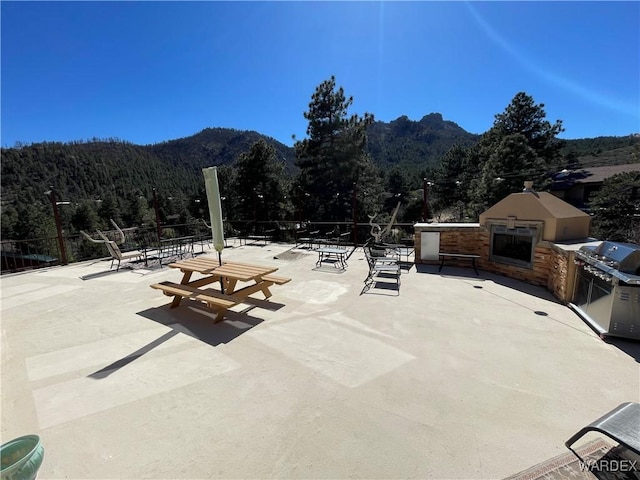 view of patio featuring a fireplace, a mountain view, a view of trees, and fence