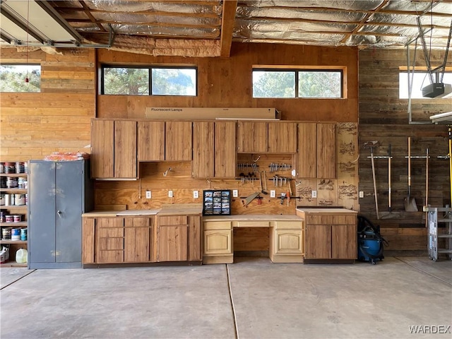 interior space featuring concrete flooring, wood walls, light countertops, hanging light fixtures, and a wealth of natural light