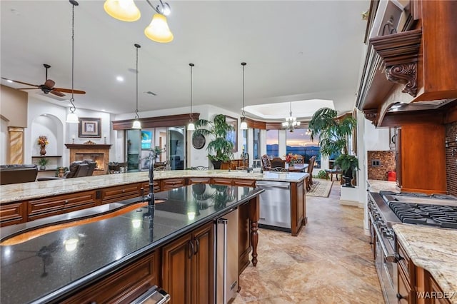 kitchen featuring decorative light fixtures, a fireplace, appliances with stainless steel finishes, open floor plan, and dark stone counters