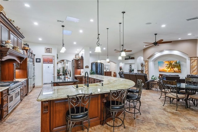 kitchen featuring arched walkways, range with two ovens, a sink, hanging light fixtures, and a large island