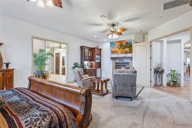 bedroom featuring a ceiling fan, visible vents, a tiled fireplace, and light colored carpet