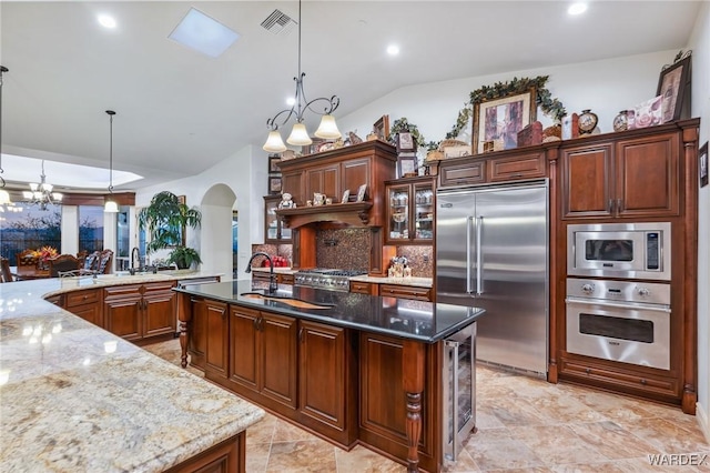 kitchen with hanging light fixtures, arched walkways, dark stone countertops, and built in appliances