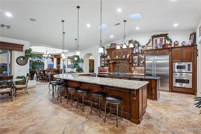 kitchen featuring visible vents, arched walkways, glass insert cabinets, built in appliances, and hanging light fixtures