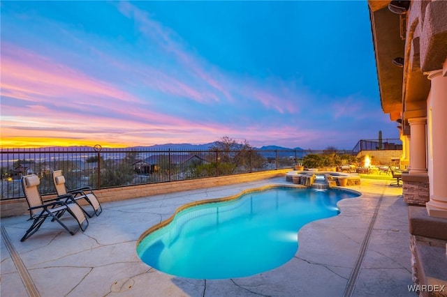 pool at dusk featuring a patio, a pool with connected hot tub, a fenced backyard, and a mountain view