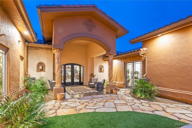 entrance to property with stucco siding, a tile roof, and french doors