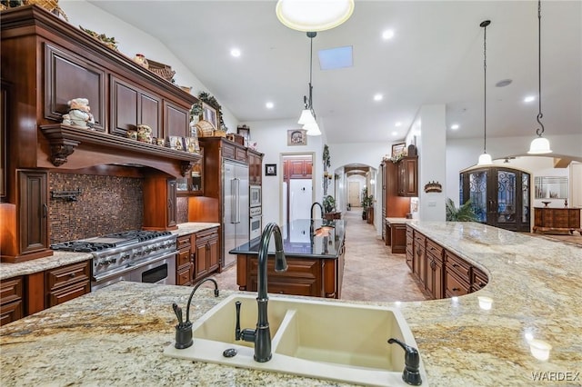 kitchen featuring arched walkways, built in appliances, light stone countertops, pendant lighting, and a sink