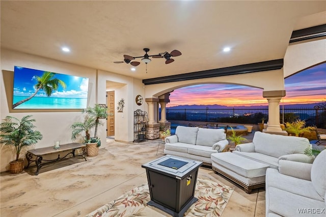 patio terrace at dusk with ceiling fan, fence, and an outdoor living space with a fire pit