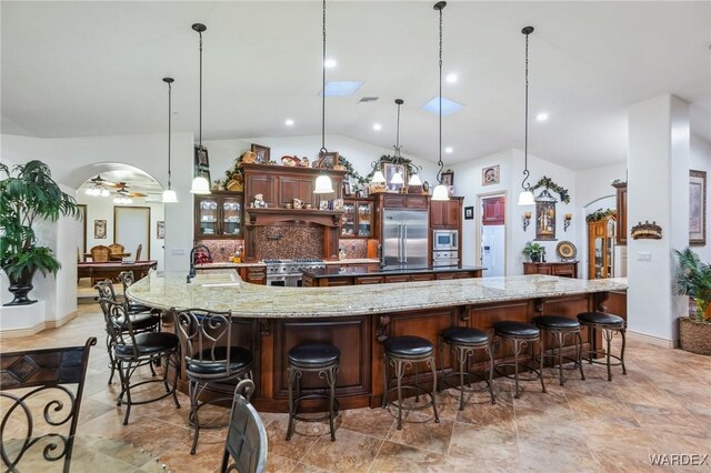 kitchen featuring glass insert cabinets, built in appliances, hanging light fixtures, a kitchen bar, and a sink