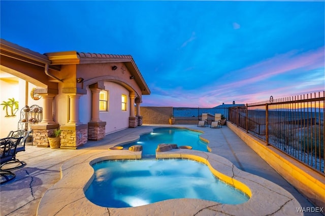 pool at dusk with a fenced backyard, a pool with connected hot tub, and a patio