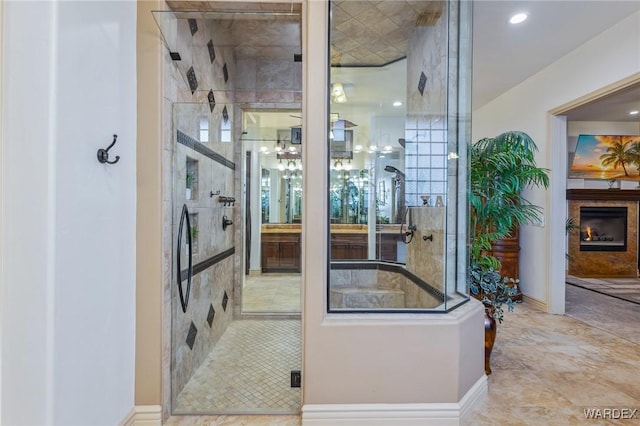 bathroom featuring a stall shower, a warm lit fireplace, and baseboards