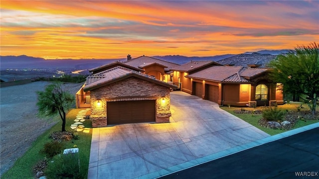 view of front of house featuring a mountain view, a garage, stone siding, driveway, and a tiled roof