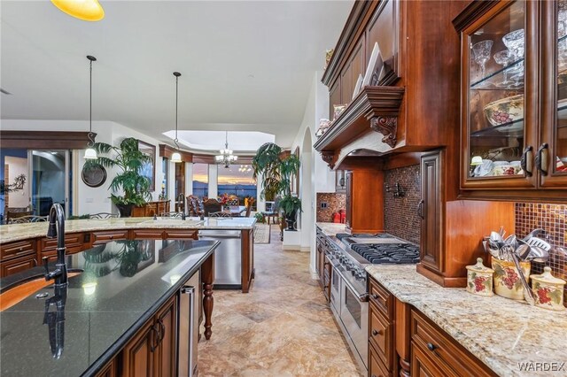 kitchen with decorative light fixtures, decorative backsplash, glass insert cabinets, appliances with stainless steel finishes, and dark stone counters