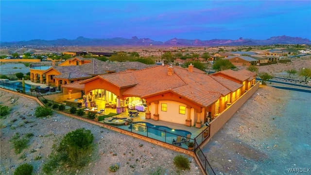 back of property at dusk with a tile roof, fence, a mountain view, and a patio