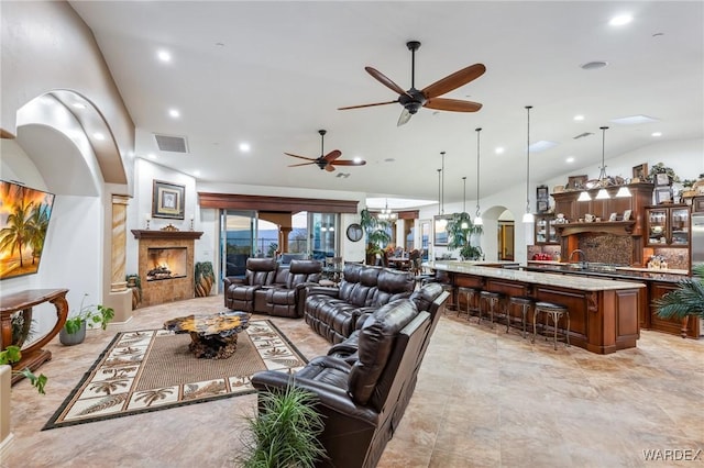 living room with arched walkways, recessed lighting, ceiling fan with notable chandelier, visible vents, and a lit fireplace