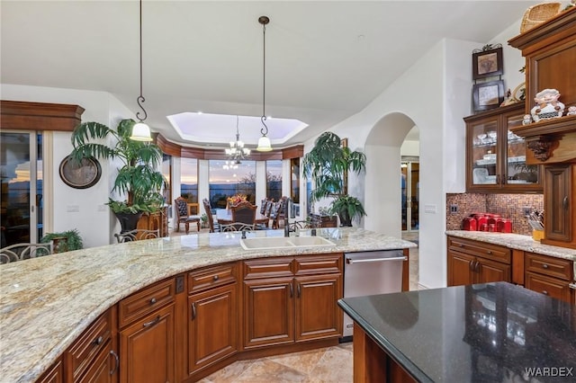 kitchen featuring glass insert cabinets, a sink, stainless steel dishwasher, light stone countertops, and decorative light fixtures