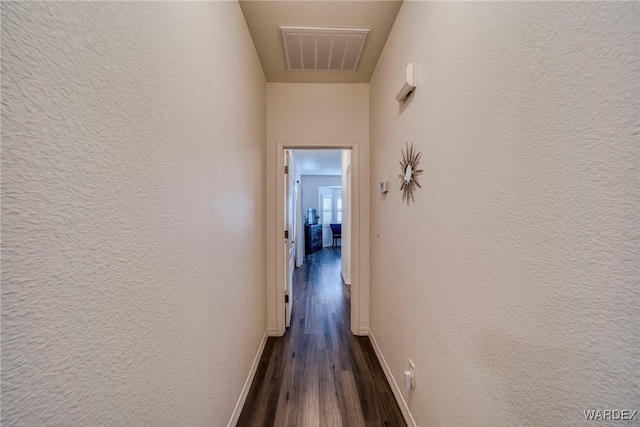 hall featuring baseboards, visible vents, dark wood-style flooring, and a textured wall