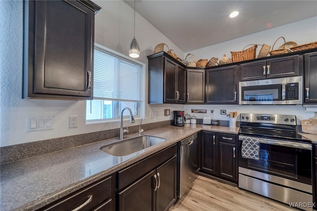 kitchen with light wood-style flooring, stainless steel appliances, a sink, dark countertops, and decorative light fixtures