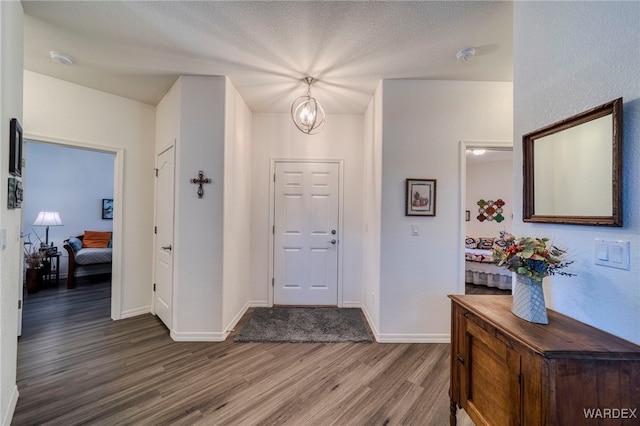 entryway with a textured ceiling, an inviting chandelier, wood finished floors, and baseboards