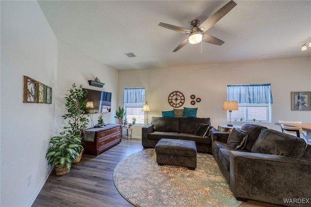 living room with ceiling fan, visible vents, baseboards, and dark wood-type flooring