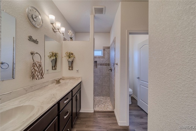 bathroom with a sink, wood finished floors, walk in shower, and toilet