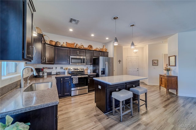 kitchen with pendant lighting, stainless steel appliances, visible vents, a kitchen island, and a sink