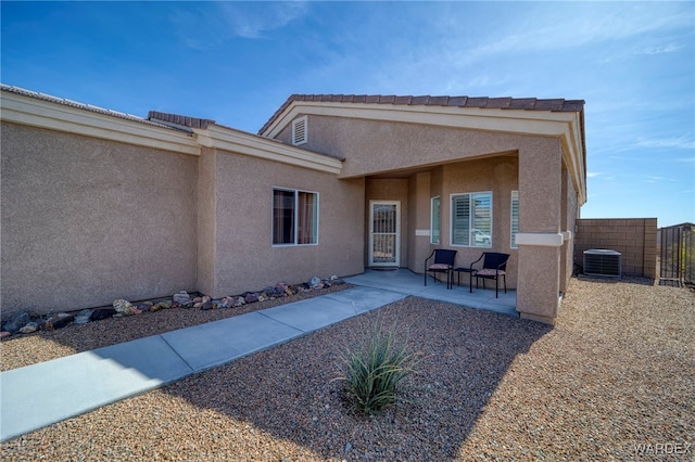 doorway to property with a patio area, fence, central AC, and stucco siding