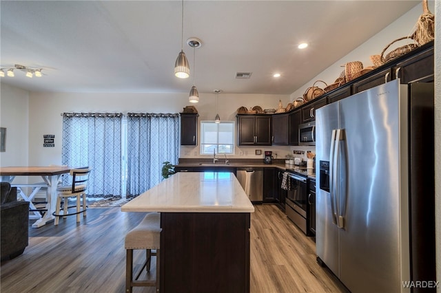 kitchen with light wood-style flooring, stainless steel appliances, a sink, a kitchen island, and hanging light fixtures