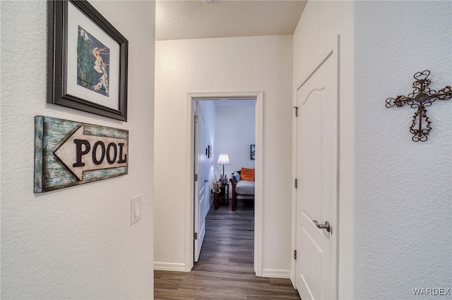 corridor with a textured wall, dark wood finished floors, and baseboards