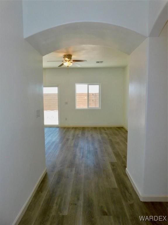 empty room with baseboards, visible vents, arched walkways, and dark wood-type flooring