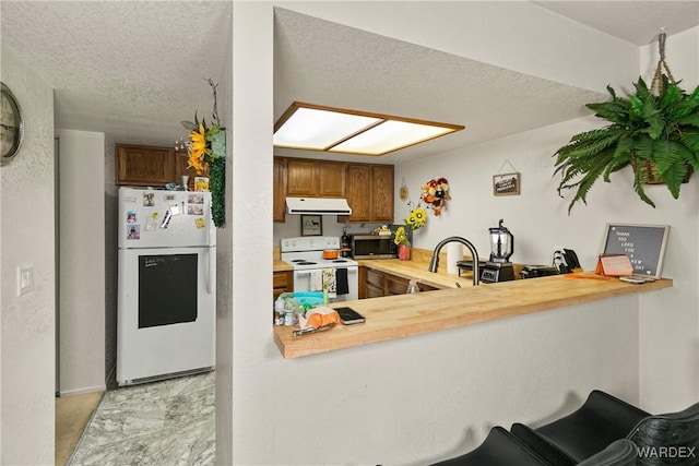 kitchen featuring white appliances, light countertops, under cabinet range hood, and a peninsula