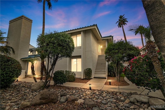 rear view of property with a chimney, stairway, and stucco siding