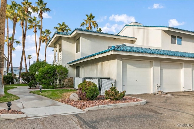 view of property exterior featuring a garage, fence, aphalt driveway, and stucco siding