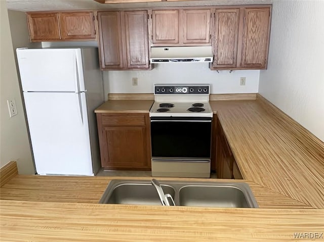 kitchen with brown cabinetry, freestanding refrigerator, electric range, and under cabinet range hood