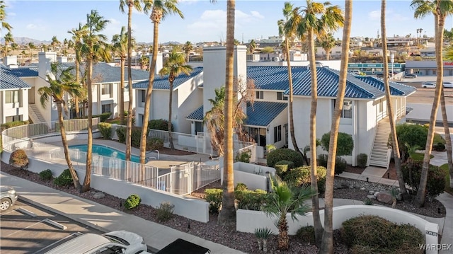 view of building exterior featuring stairs, fence, a residential view, and a community pool