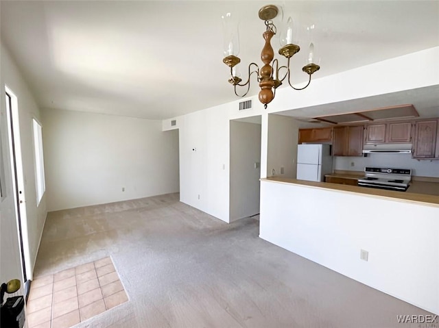 kitchen with pendant lighting, brown cabinets, electric range, freestanding refrigerator, and under cabinet range hood