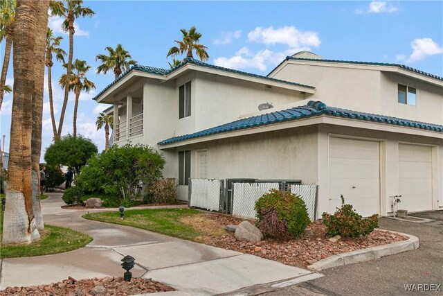 view of property exterior with a garage, a tiled roof, fence, and stucco siding