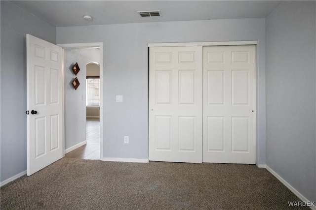 unfurnished bedroom featuring visible vents, a closet, baseboards, arched walkways, and carpet flooring