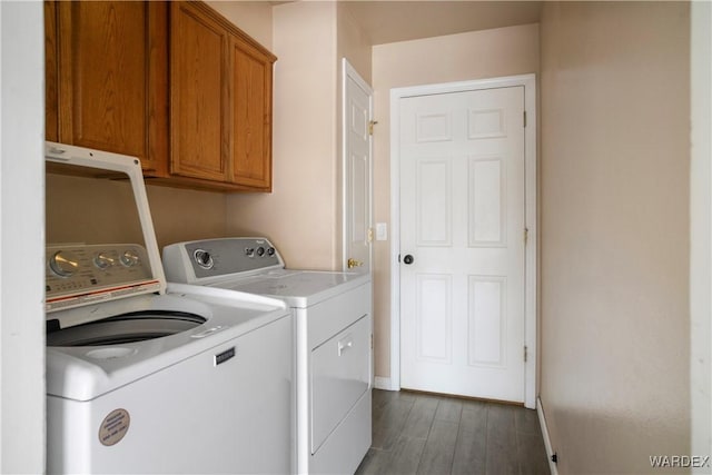 washroom featuring cabinet space, baseboards, washing machine and dryer, and dark wood-type flooring