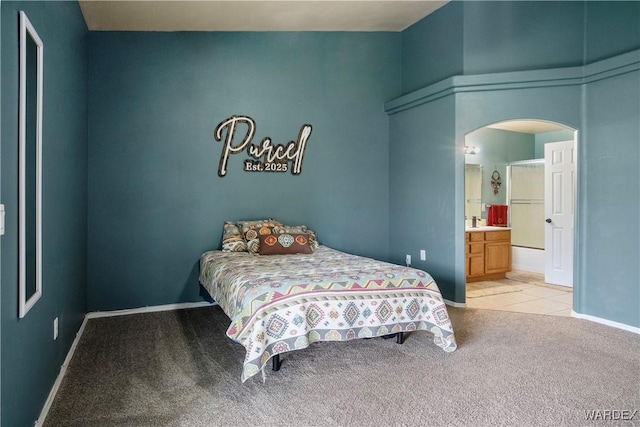 bedroom with baseboards, arched walkways, ensuite bath, and light carpet