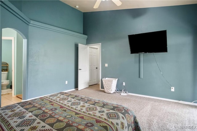 bedroom with a towering ceiling, light carpet, baseboards, connected bathroom, and arched walkways
