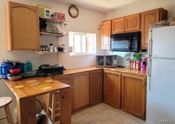 kitchen featuring brown cabinets, black microwave, light countertops, and freestanding refrigerator