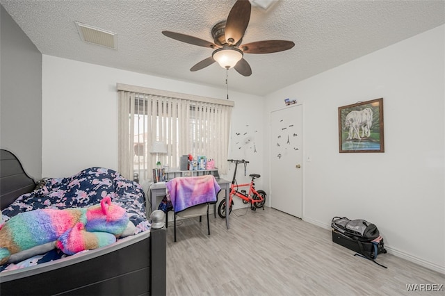 bedroom with a textured ceiling, ceiling fan, wood finished floors, and visible vents