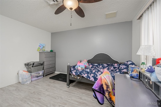 bedroom with a ceiling fan, visible vents, light wood-style flooring, and a textured ceiling